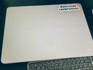 My Surface Studio Laptop, with a sticker saying #include everyone' in rainbow text stuck to the top right corner