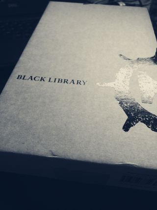 A black-and-white photo of plain cardboard book packaging, featuring Black Library branding printed in black
