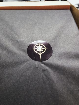 Black tissue paper wrapped around a book. The wrapping is secured with a sticker featuring a stylised compass evocative of a star.