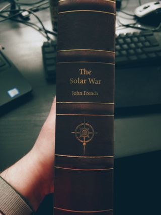 A red leather book spine, featuring embossing and the same compass/star design as the cover, but in gold. The title, Solar War, and author name, John French, are also picked out in gold lettering, and positioned above the compass