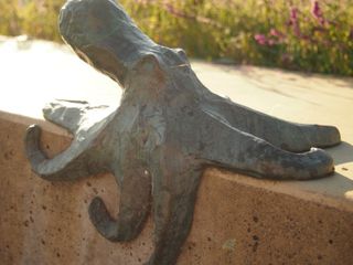 A bronze sculpture of an octopus, attached to a wall. The sculpture is covered in dark green verdigris, which is worn away in some places to reveal the natural orangey-brown of the metal.