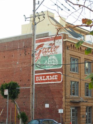 A vintage, well-worn, sign painted on the side of a red-brick wall. It advertises Gallo Salame, and features a stylised illustration of a tram car
